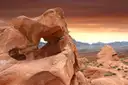 A red sandstone arch in Valley of Fire State Park under an orange evening sky