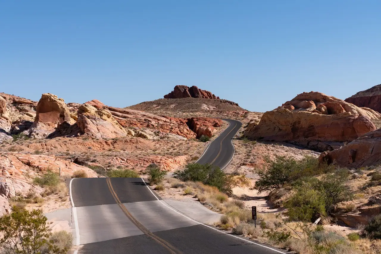 A road winding between red and cream sandstone rocks in Valley of Fire under a clear sky